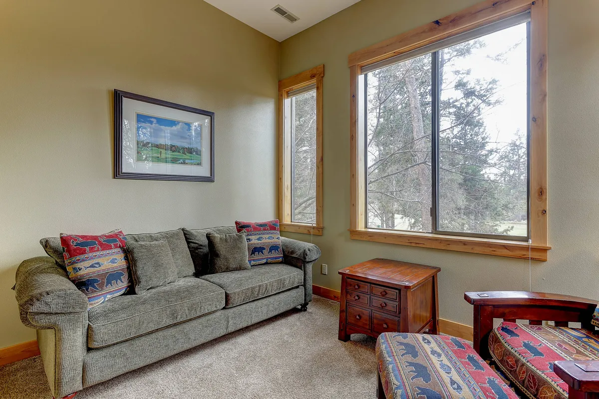 A cozy living area with a sofa featuring patterned cushions, a wooden side table, and large windows that frame an inviting outdoor view. The scene offers a restful spot to relax after outdoor adventures with your dog.