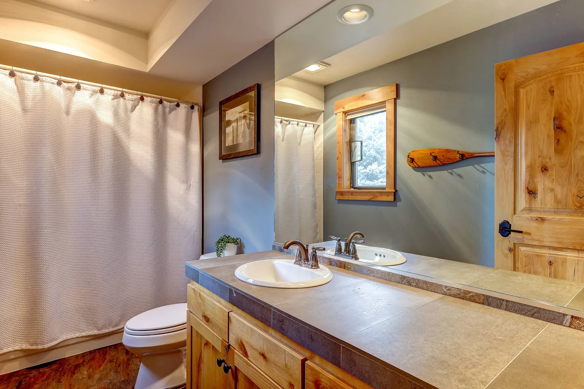 A spacious double sink vanity set against natural light streaming through a window. A wooden paddle on the wall adds a touch of the outdoors and adventure, while neatly arranged towels evoke a sense of order and readiness.