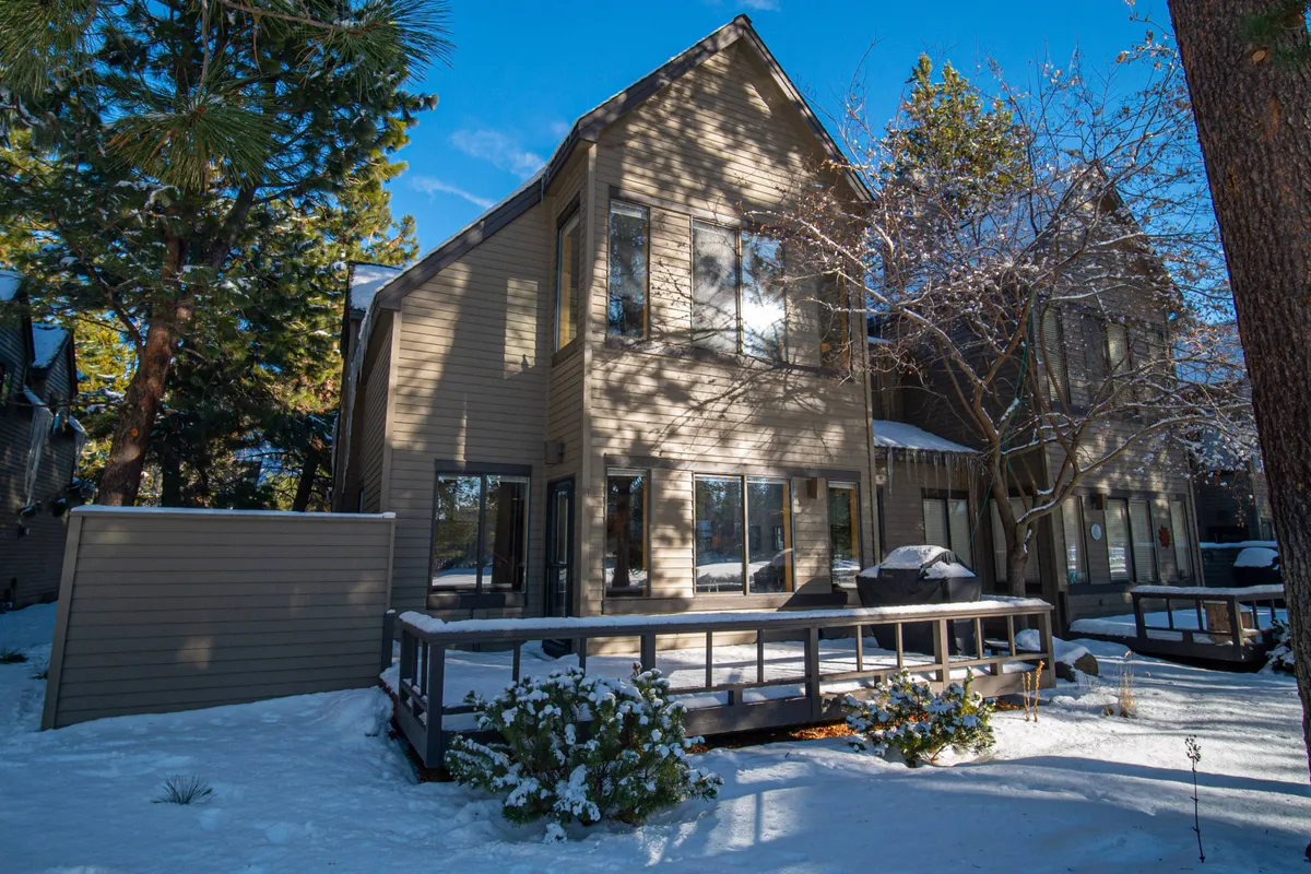A serene view of the home's exterior shows snow-covered ground surrounding a wooden deck, framed by large windows and towering trees. The peaceful landscape connects the property to nature and the outdoors, offering an inviting setting for relaxation or romantic stargazing.