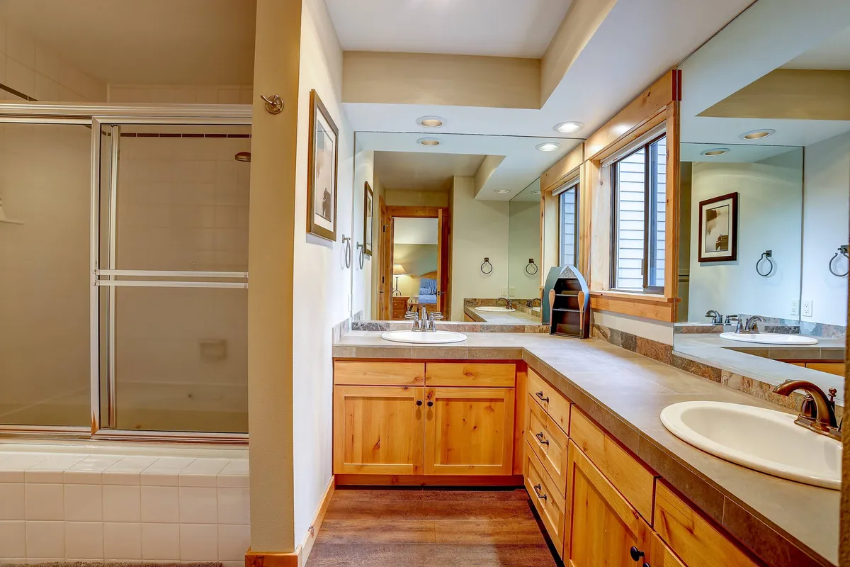 A modern bathroom with a double vanity sink, spacious shower area, large mirrors, and wood cabinetry. The space is bright, fresh, and ideal for relaxing self-care routines.