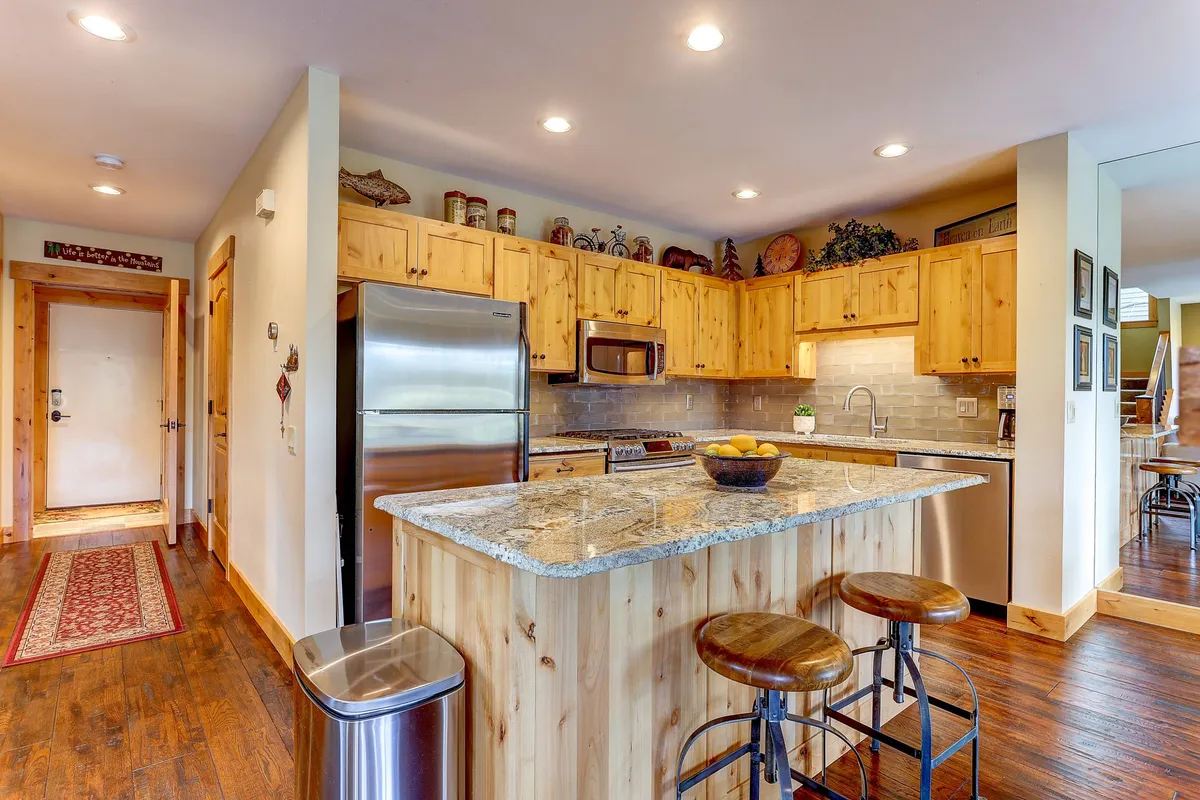 A modern kitchen with granite countertops, wooden cabinets, stools for casual seating, and sleek stainless steel appliances. The kitchen is designed for both style and function, making it a hub for cooking and entertaining.