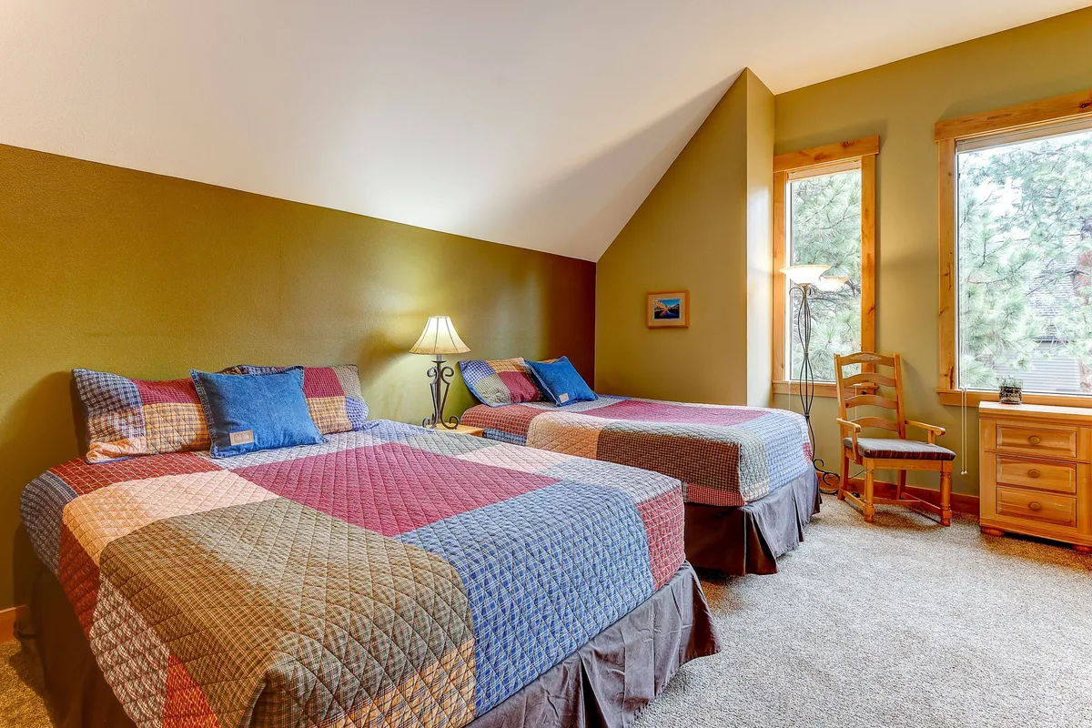 A guest bedroom with two beds, windows offering natural light, a lamp, a chair, and a dresser. The room feels welcoming and versatile, ideal for extra guests or family members.